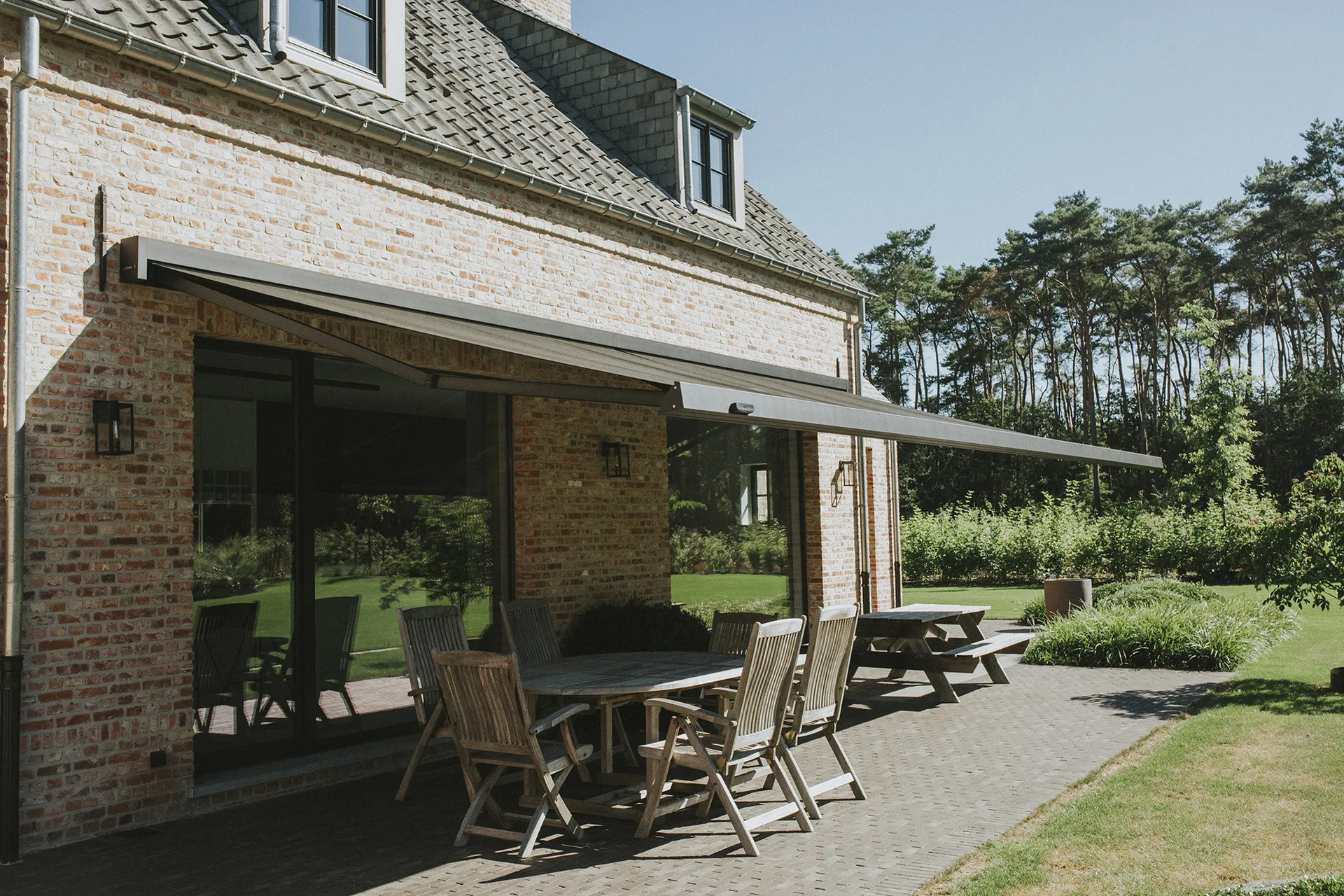 Knikarmscherm uitgeklapt boven het terras van een woonhuis