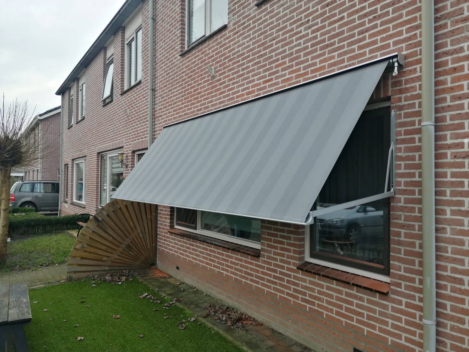 Uitvalscherm met gestreept doek uitgeklapt boven een raam