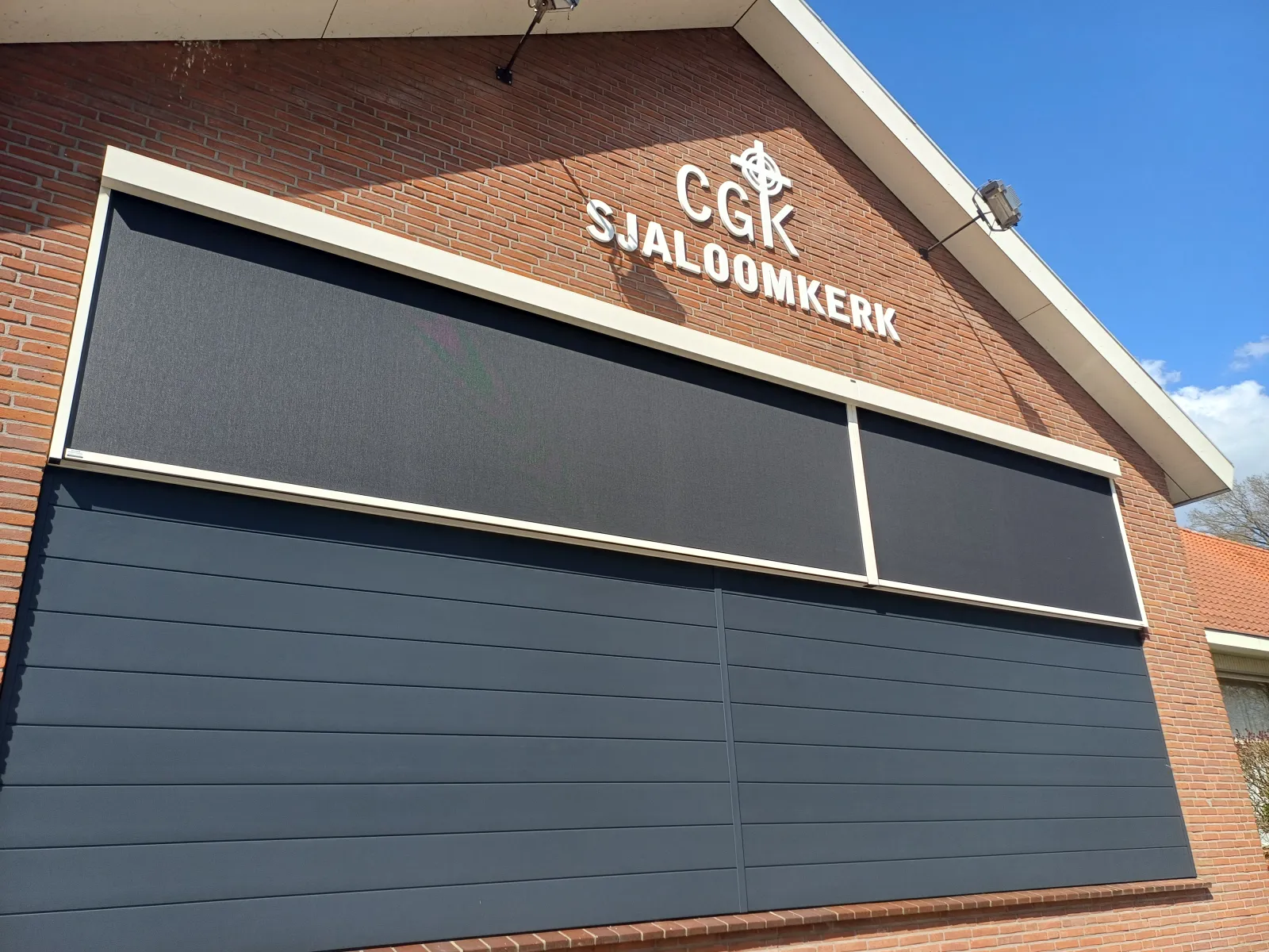 Kerkgebouw met rolluiken en screens over de volle gevelbreedte